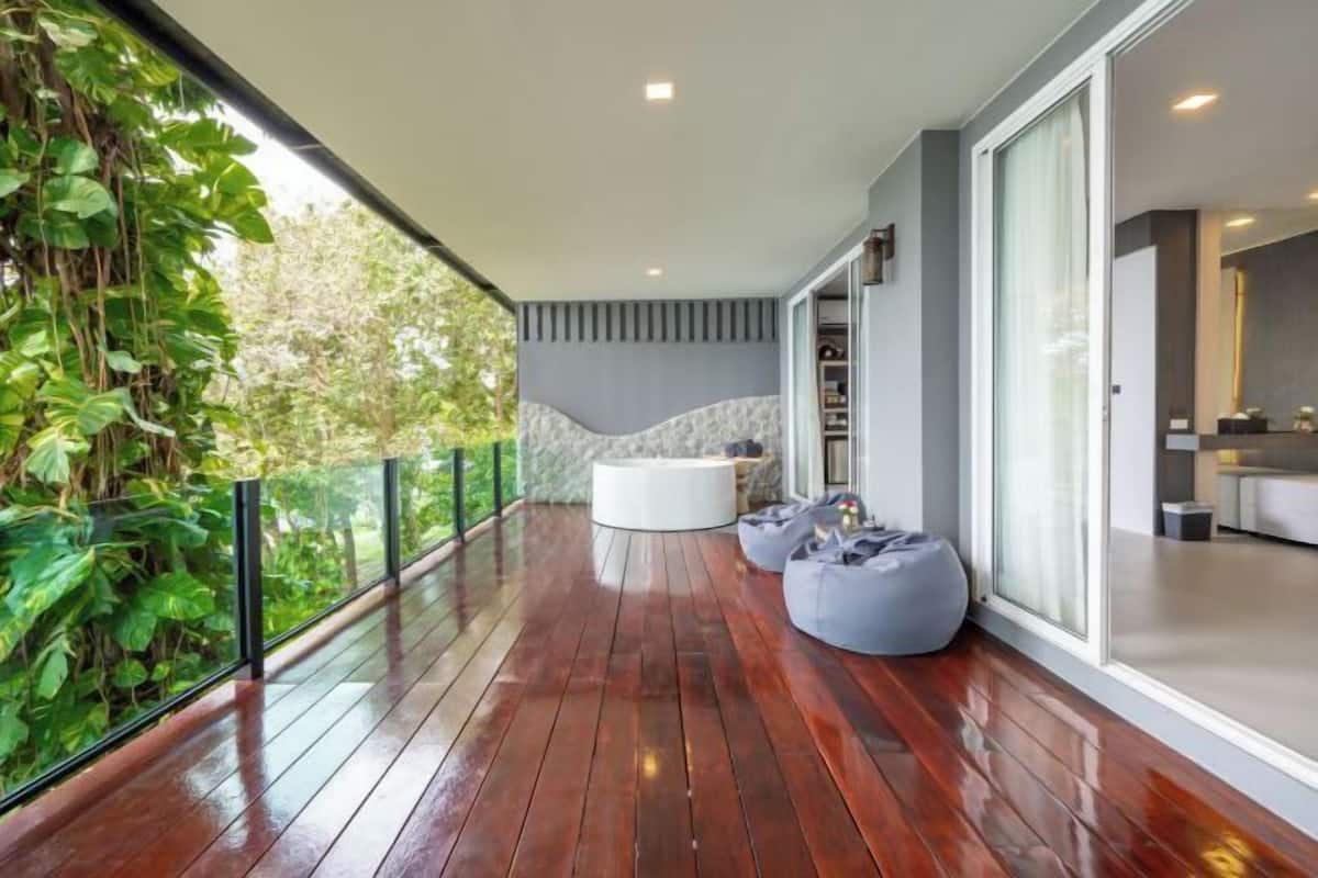 A modern balcony with wooden flooring, a white round seating area, and a glass door leading to a kitchen.