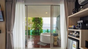 A modern room with a sliding glass door leading to a balcony, a round seating area, and a kitchenette. - Anona Sunset Boutique (Phuket)