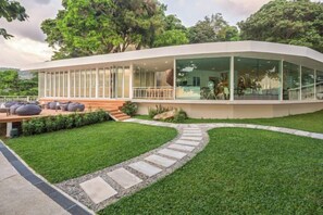 A modern building with a curved facade, large windows, and a grassy courtyard with seating. - Anona Sunset Boutique (Phuket)