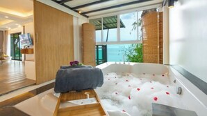 A modern spa room with a large bathtub filled with bubbles, a wooden bench, and a view of the sea through large windows. - Anona Sunset Boutique (Phuket)