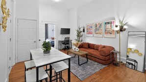 A modern living room with a white sofa, a dining table with chairs, a TV mounted on the wall, and artwork. - 1/1 Center City Sleeps 6 Fast Wifi (Philadelphia)