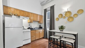 A modern kitchen with wooden cabinets, a white refrigerator, and a dining area with a marble table and chairs. - 1/1 Center City Sleeps 6 Fast Wifi (Philadelphia)