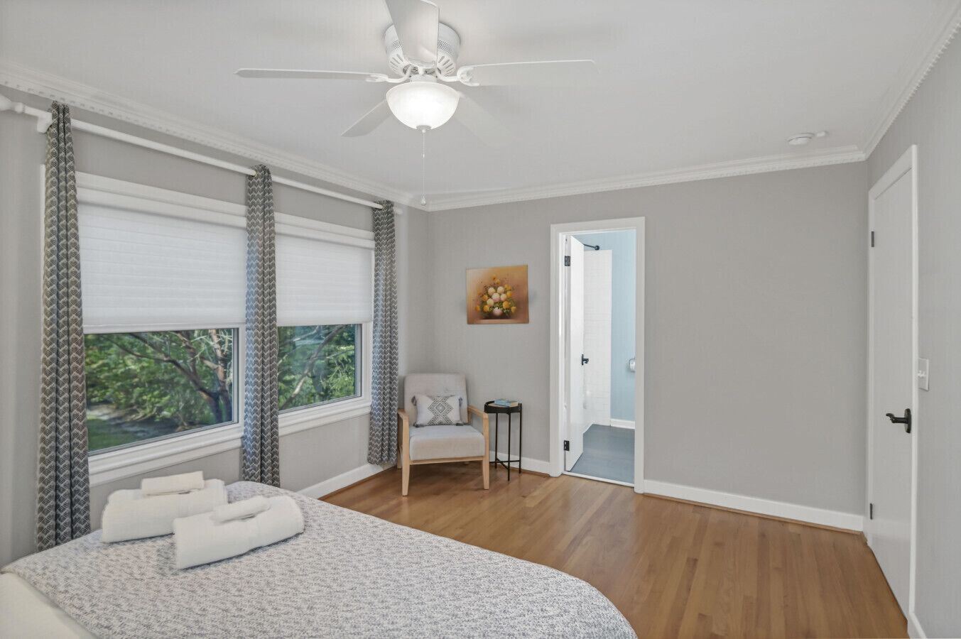 Une chambre à coucher comprenant un lit, une chaise, un ventilateur de plafond et une porte donnant sur une autre pièce.