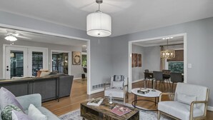 A modern living room with a grey sofa, a wooden coffee table, and a dining area with a white table and chairs. - Forest Lake Retreat | Backyard Sanctuary & Hot Tub (Columbia)