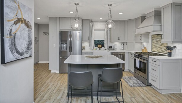 A modern kitchen with a central island, stainless steel appliances, pendant lighting, and a large abstract painting on the wall. - Forest Lake Retreat | Backyard Sanctuary & Hot Tub (Columbia)