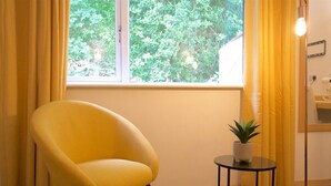 A yellow armchair by a window with yellow curtains, a small table with a plant, and a floor lamp. - Country pub with rooms (Shenstone)