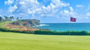 Un campo de golf con una bandera en el green, un acantilado y el océano al fondo.