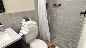 Kylpyhuone, jossa on wc, pesuallas, lasiovilla varustettu suihku ja pyyhekoukku.