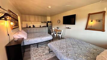 A compact room with two beds, a small kitchenette, a dining area, and a TV.