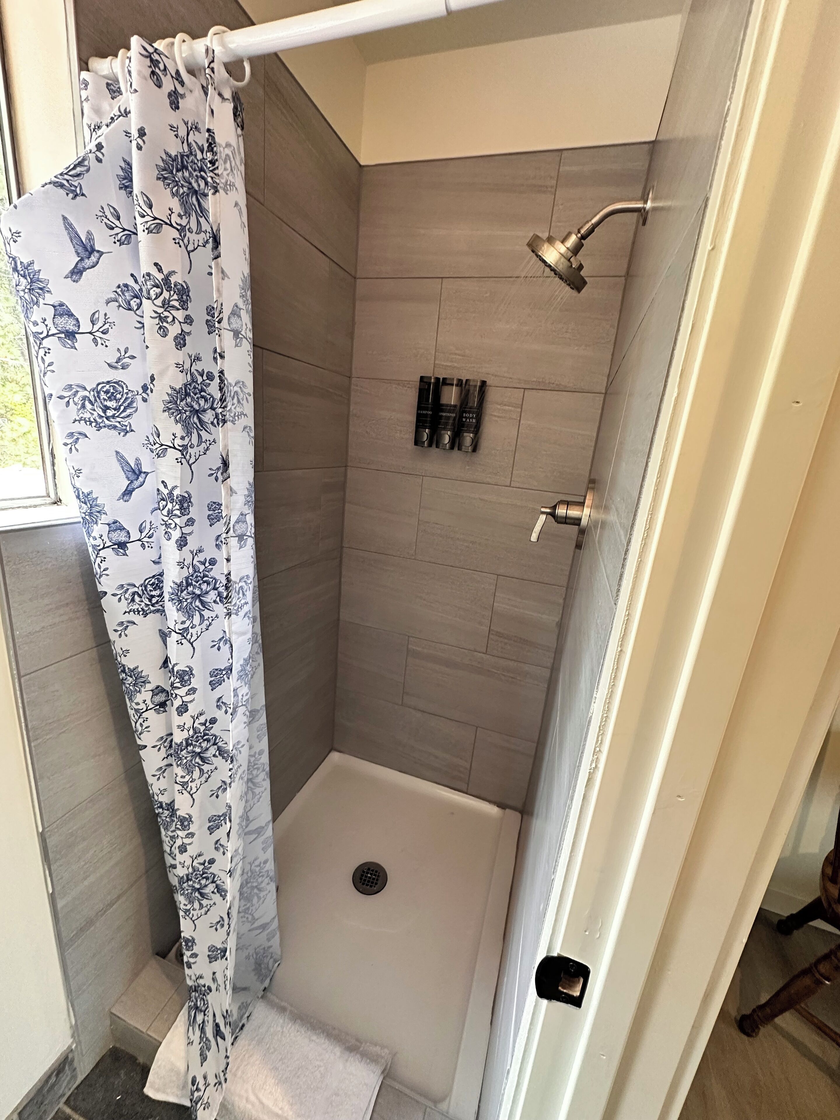 Eine Dusche mit Blumenmuster-Vorhang, eine Duschbrause zum Anschließen und ein kleines Regal mit Toilettenartikeln.