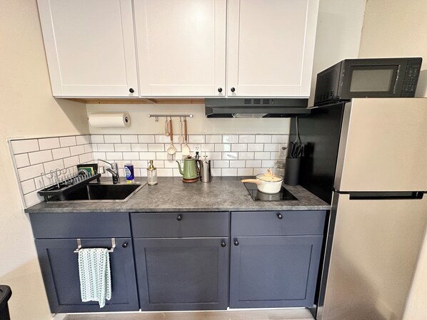 A kitchen with white cabinets, a black countertop, a stainless steel refrigerator, and a microwave. - Basecamp (Sagle)