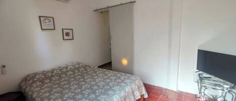 A bedroom with a bed, an air conditioner, a TV, and a red tiled floor.