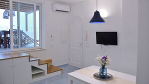 A modern interior with a staircase, a flat-screen TV, and a vase with flowers. - In an old fishing village apartment with sea view terrace (Ischia)