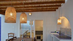 A dining area with a wooden table and chairs, a kitchen visible through an archway, and hanging wicker lamps. - In an old fishing village apartment with sea view terrace (Ischia)