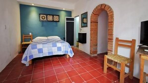 A bedroom with a bed, a chair, a TV, and a brick archway.
