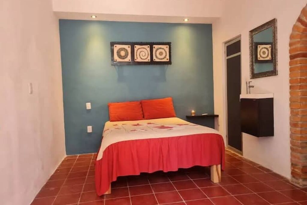 A bedroom with a bed, a nightstand, a mirror, and a wall-mounted shelf.