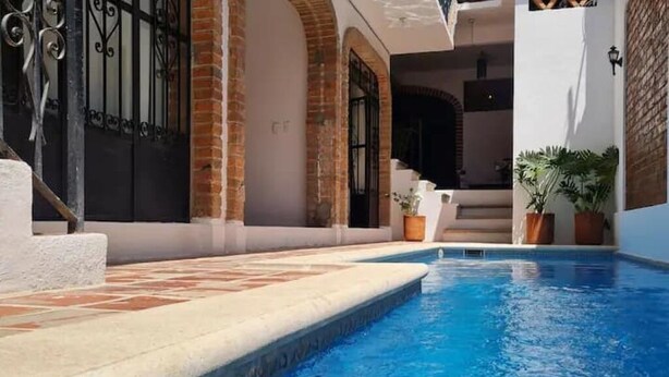 A swimming pool with a tiled deck, brick walls, and a metal gate.