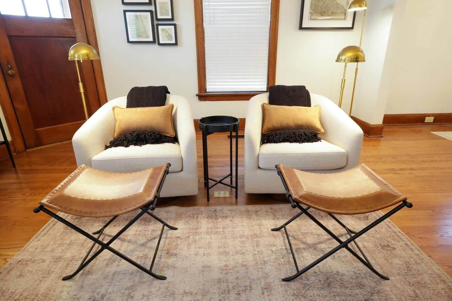 Un salon avec deux fauteuils blancs, une petite table d’appoint noire et un tapis à motifs.