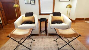 Un salon avec deux fauteuils blancs, une petite table d’appoint noire et un tapis à motifs.
