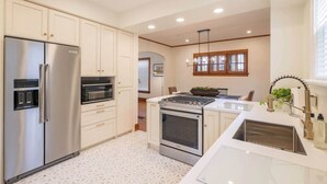 A modern kitchen with stainless steel appliances, white cabinetry, and a patterned floor. - Riggs House Restored 1908 Home (Maquoketa)