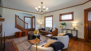 A spacious living room with a staircase, a chandelier, and a cozy seating area. - Riggs House Restored 1908 Home (Maquoketa)