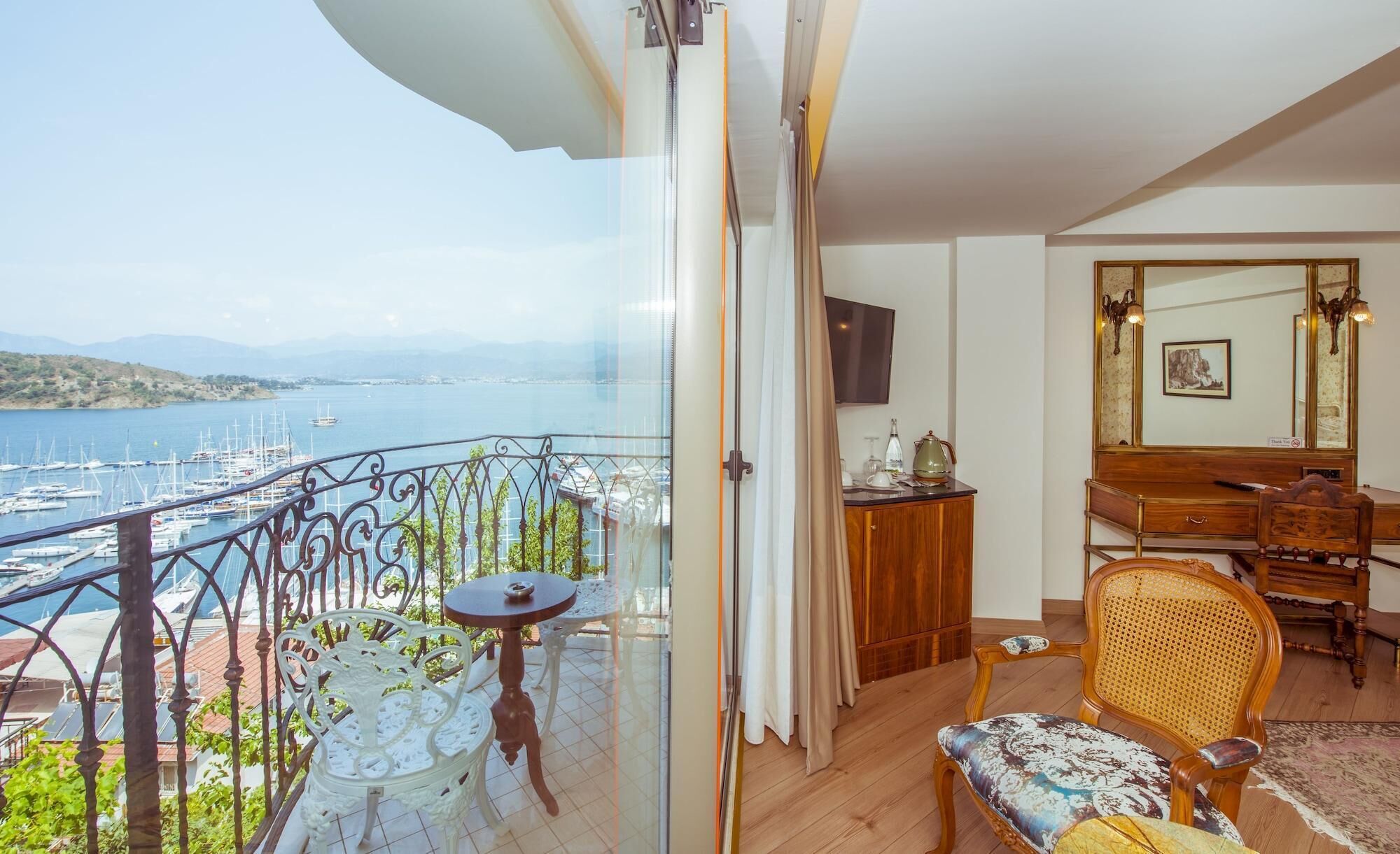A balcony with a view of a marina and boats, a wooden dresser, a television, and a wicker chair.