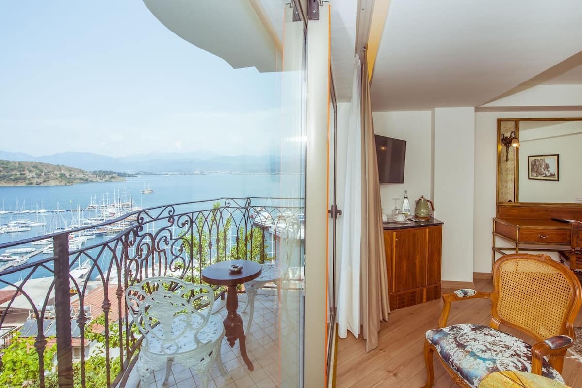A balcony with a view of a marina and boats, a wooden dresser, a television, and a wicker chair.