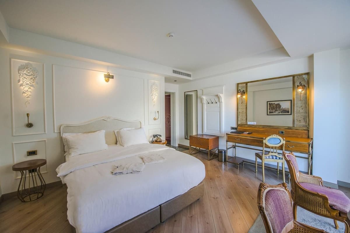 A bedroom with a large bed, a wooden dresser, a chair, and a mirror.