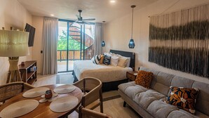 Habitación de hotel con cama, sofá, mesa de comedor con individuales, lámpara y ventilador de techo.