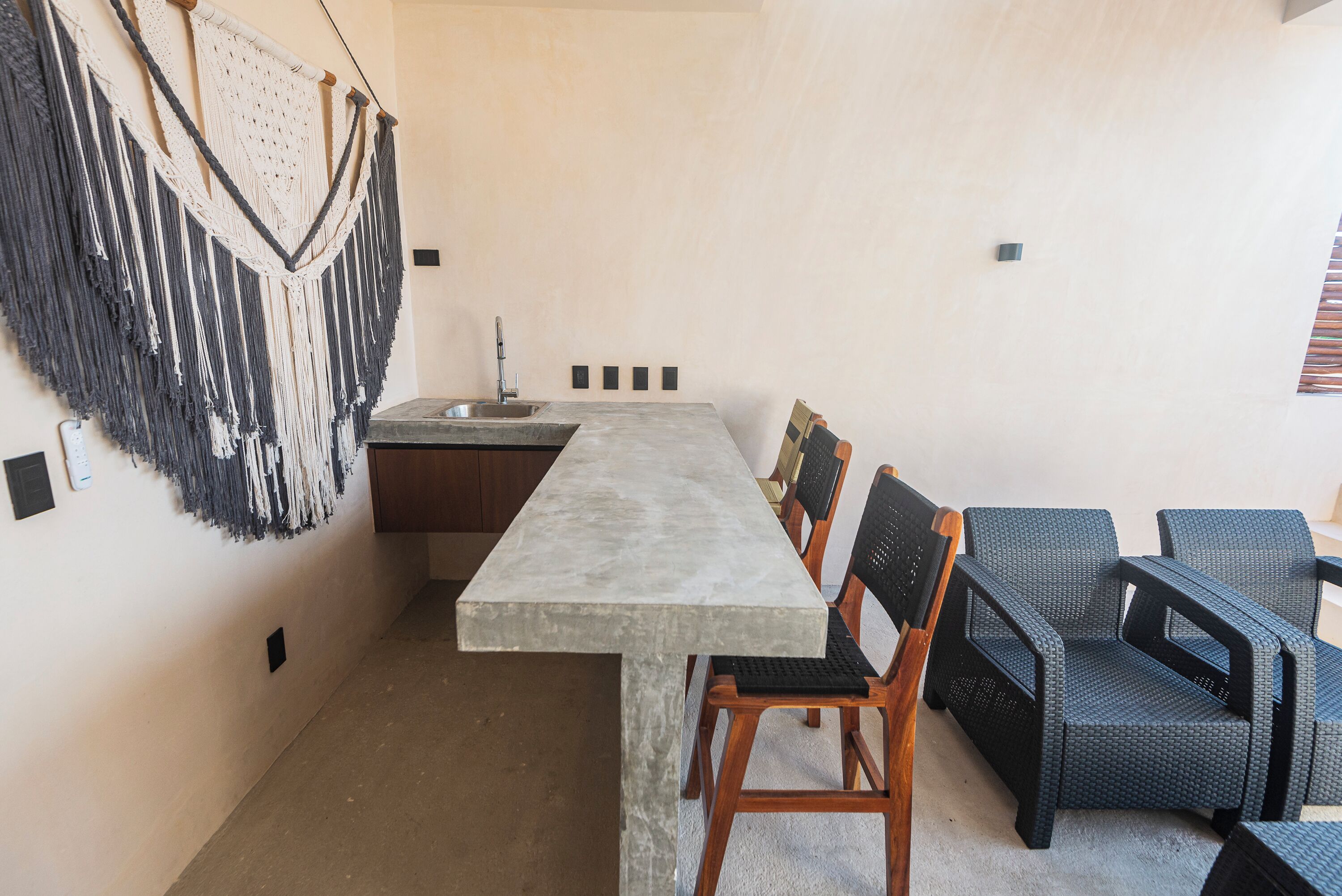 Eine moderne Küche mit einer großen Kochinsel, Holzstühlen und einem Wandbehang aus Makramee.