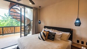Un dormitorio con cama, almohadas, una mesita de noche, un ventilador de techo y una escalera de caracol que lleva a un balcón al aire libre.
