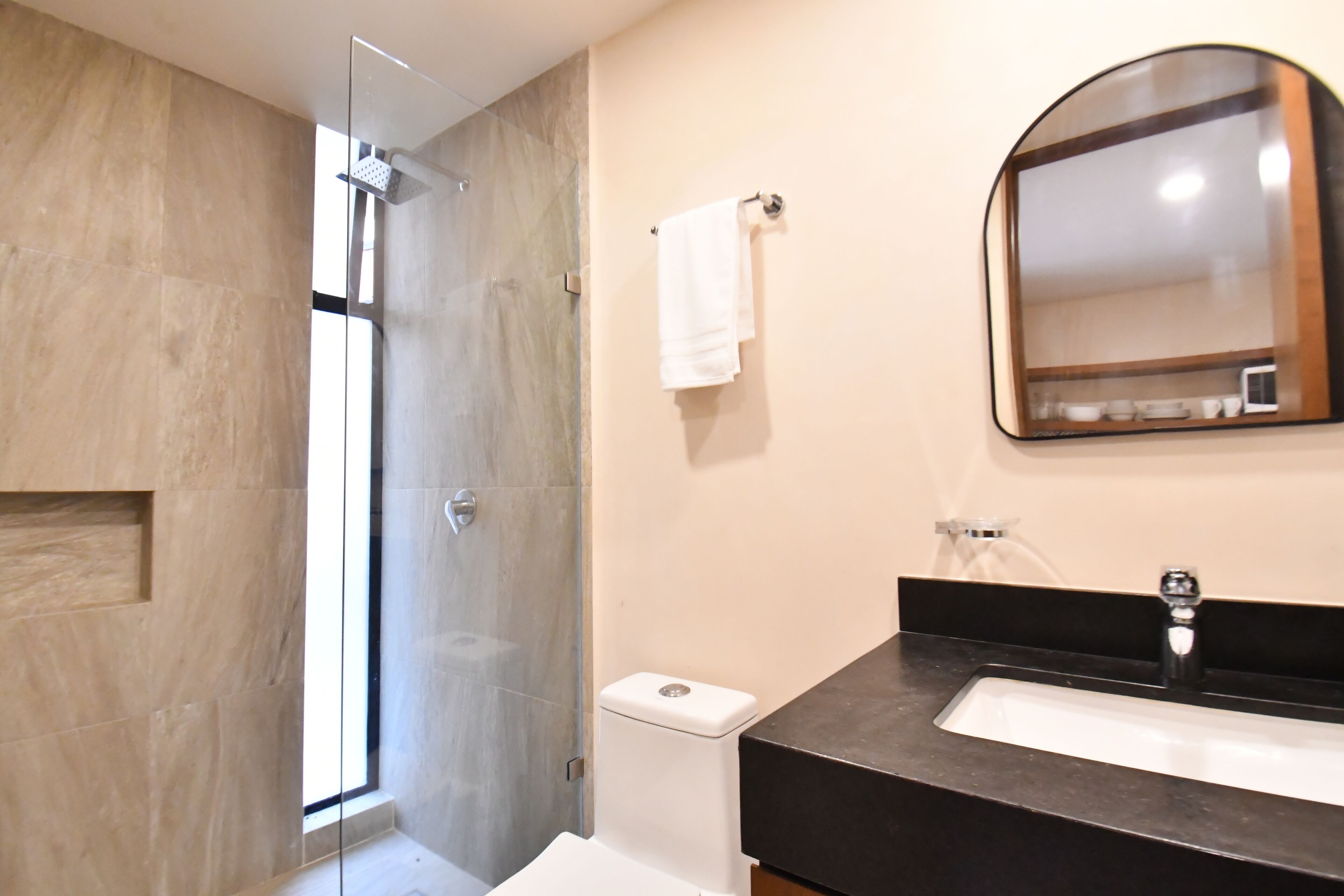 Une salle de bain moderne avec une douche à l’italienne en verre, des toilettes blanches et un plan de toilette noir avec un lavabo.