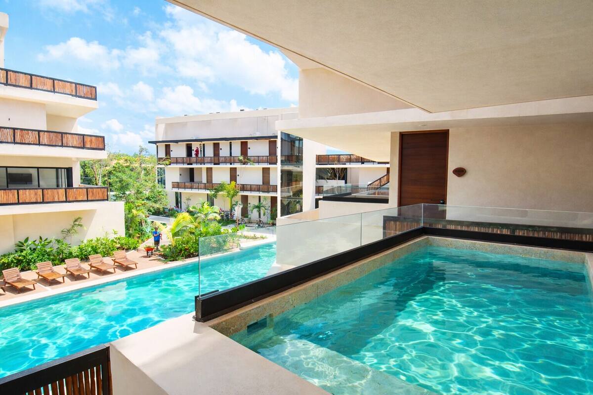 A pool area with lounge chairs, a clear pool, and a multi-story building with balconies.