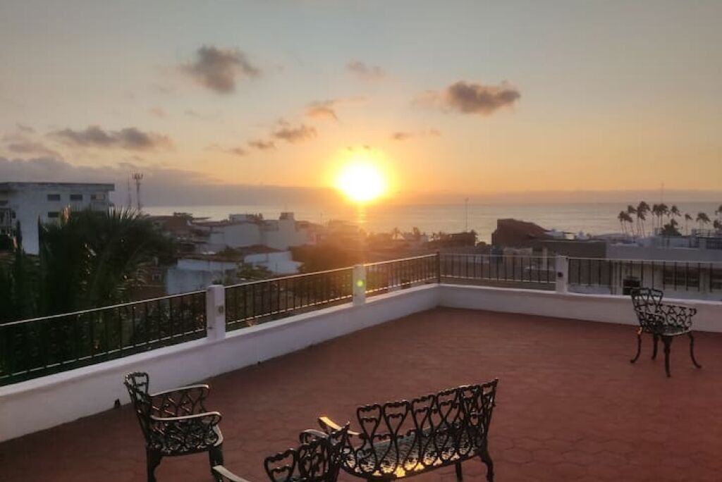 Terraza en la azotea con vista al atardecer, con dos sillas de metal y una mesa pequeña.