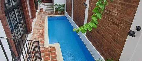 Una piscina stretta con bordo piastrellato, circondata da muri in mattoni e un cancello in metallo.