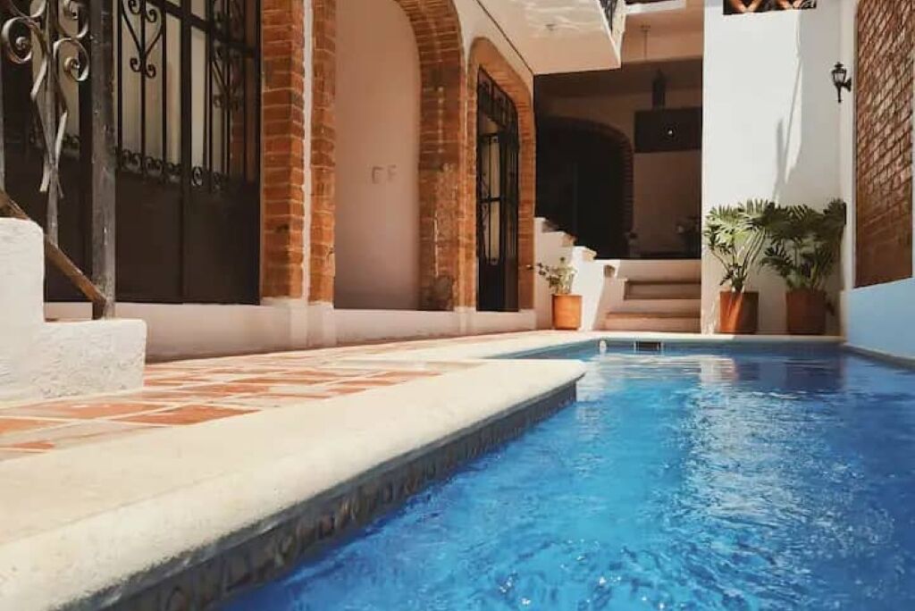 A swimming pool with a tiled deck, brick walls, and a metal gate.