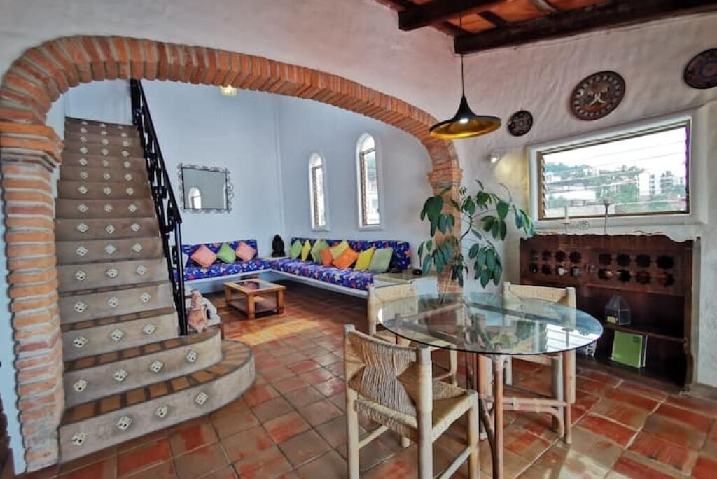 A living room with a brick staircase, a glass table, and a blue sofa with colorful cushions.