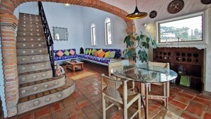 Een woonkamer met een stenen trap, een glazen tafel en een blauwe bank met kleurrijke kussens.