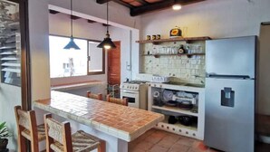Een keuken met een betegeld eiland, houten stoelen, een fornuis, een koelkast en hangende lampen.