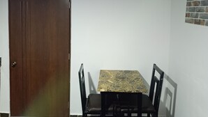 Une pièce avec une porte en bois, une table avec des chaises, un climatiseur et un téléviseur fixé au mur.