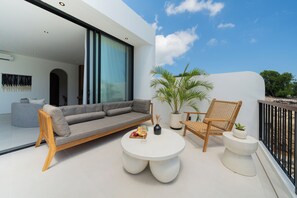 Et moderne udeområde med en sofa, runde borde, stole, en potteplante og udsigt til himlen.