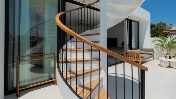 A modern spiral staircase with wooden steps and black railings, leading to an open-plan living area with a large sliding glass door. - Modern 3br Villa with Rooftop Patio - Pool Table (South Kuta)