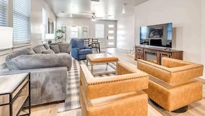 A spacious living room with a sofa, armchairs, a coffee table, and a TV.