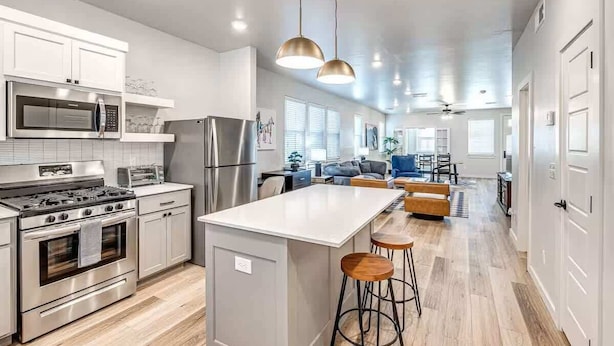 A modern kitchen with stainless steel appliances, a central island with stools, and pendant lighting.