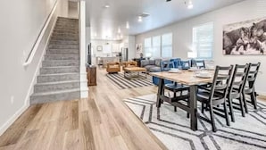 A spacious living area with a staircase, a dining table with chairs, a sofa, and a ceiling fan.