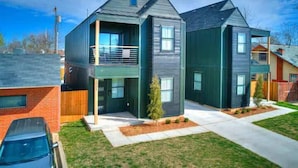 A modern two-story house with a balcony, a small front yard, and a car parked in the driveway.