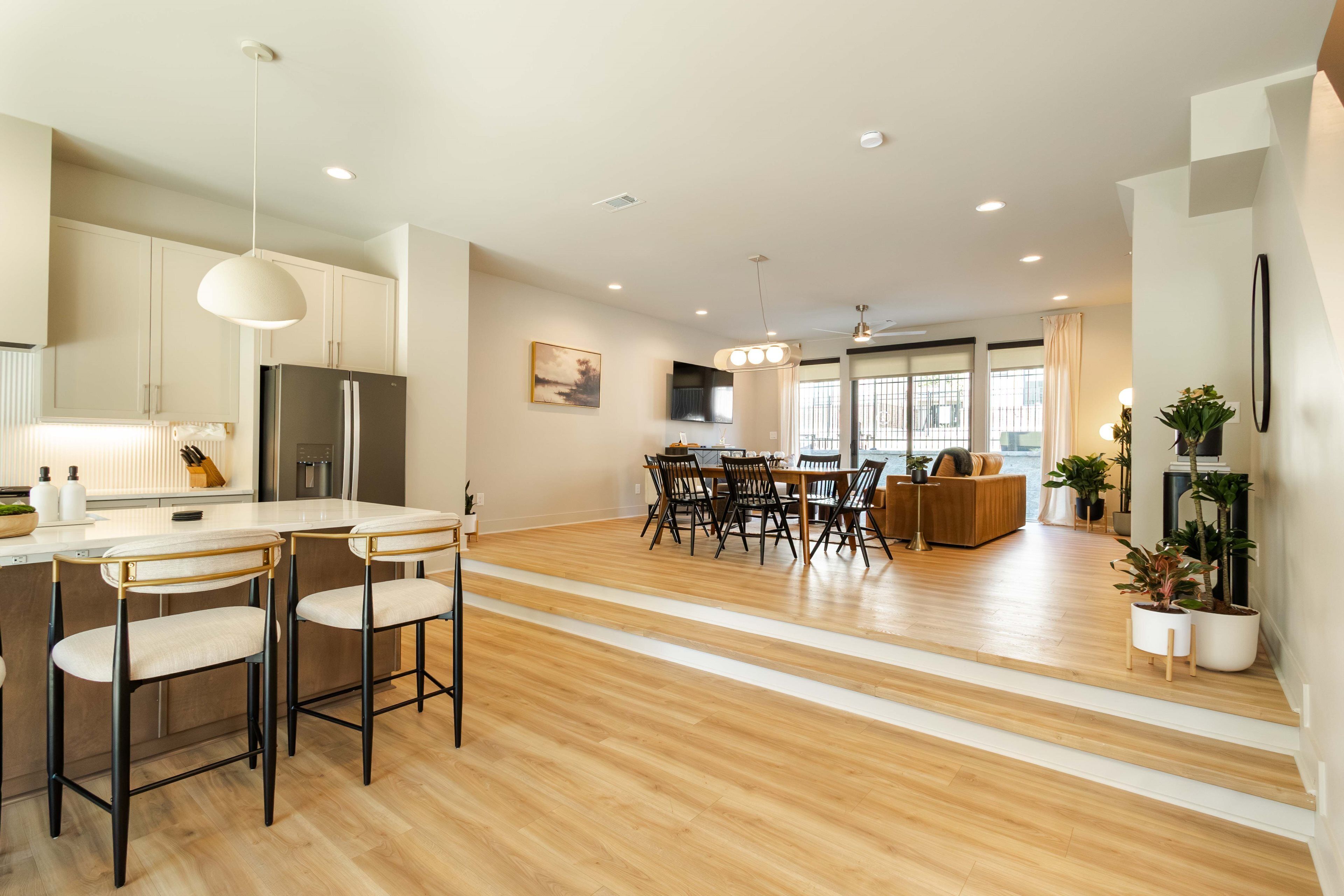 A modern kitchen with a central island, bar stools, and a dining area with a wooden table and chairs.