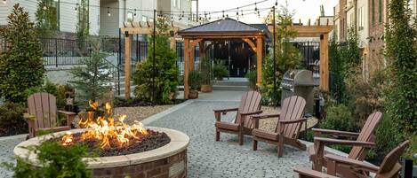 Een terras buiten met een vuurkuil, Adirondack-stoelen en een pergola.