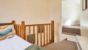 Ein Schlafzimmer mit einem hölzernen Kopfteil, einem Bett mit Kissen in Streifenmuster, einer grünen Tagesdecke und einem gerahmten Bild an der Wand.