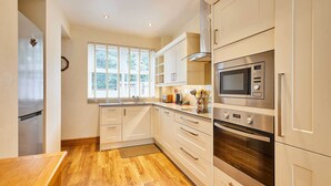 A modern kitchen with stainless steel appliances, white cabinetry, and a wooden floor. - Host Stay The Station Cottage (Rowlands Gill)